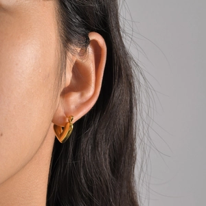 Close-up of a polished gold heart-shaped earring worn by a model on a neutral background