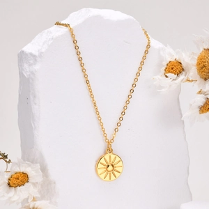 Gold stainless steel necklace with sunburst pendant displayed on white textured stones