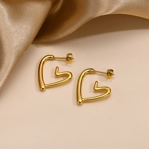 Close-up of golden hollow heart stud earrings on elegant silk fabric background