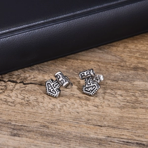 Macro detail of vintage Mjolnir stud earrings featuring intricate Norse rune engravings
