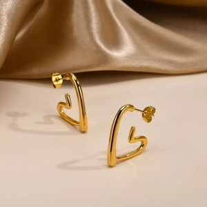 Close-up of golden irregular heart stud earrings on elegant silk background fabric
