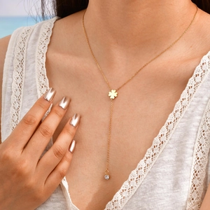 Detail of 18K gold-plated Y-necklace featuring a clover charm and zircon tassel on model