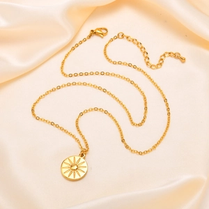 Detail of golden stainless steel sun pendant necklace on cream silk fabric background