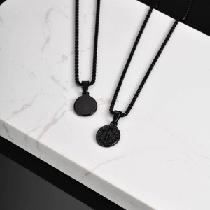 Close-up of black stainless steel cross pendant and round dog tag on marble stand