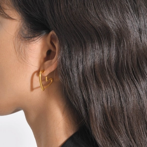 Close-up of a gold heart-shaped hoop earring worn on a model with long dark hair