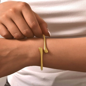 Gros plan d'un bracelet ouvert doré minimaliste en forme de goutte au poignet