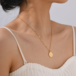 Elegant gold-tone sunburst coin pendant necklace worn with white camisole