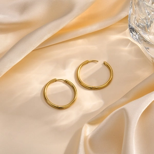 Gros plan de boucles d'oreilles créoles dorées polies sur fond de satin de soie