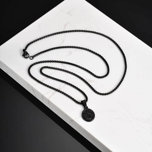 Macro view of a matte black cross embossed oval pendant necklace on white marble