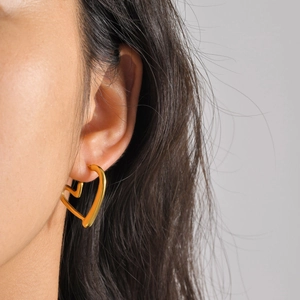 Close-up of golden hollow heart-shaped earrings on model with refined metallic texture