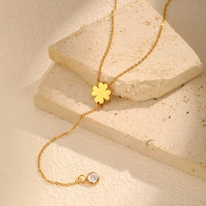 Detail of 18K gold plated clover necklace with zircon tassel on a textured stone base