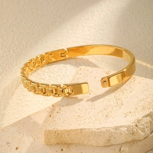 Polished 18K gold-plated watchband style bangle on natural beige stone background