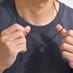 Detail of men's black oval cross pendant necklace worn on a dark grey t-shirt texture