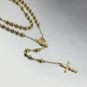 Long gold beaded chain necklace with crucifix pendant and Virgin Mary icon on metal background