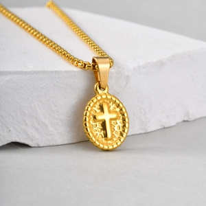 Detail of gold oval cross pendant necklace featuring relief and textured bead edge