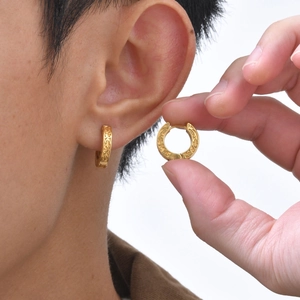 Detailed close-up of a golden engraved hoop earring with intricate floral scroll patterns