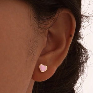 Close-up of a pink heart stud earring with gold plating worn on a model's ear