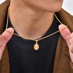 Close-up of a gold oval cross pendant necklace worn with a box chain on a model