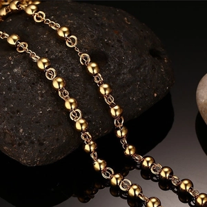 Polished gold stainless steel bead chain necklace displayed on black volcanic rock stones