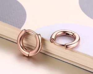 Gros plan de boucles d'oreilles créoles polies en or rose avec fermoir à charnière