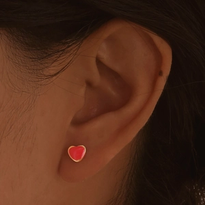 Close-up of red enamel heart stud earring with gold edges worn on the earlobe