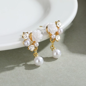 Elegant gold-plated camellia earrings with white pearls and crystals on a white ceramic plate