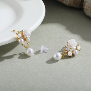 Detail view of gold camellia earrings with white pearls and sparkling rhinestones