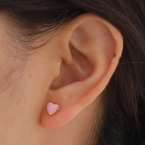 Pink heart stud earring with gold metal frame and enamel finish on a model's ear
