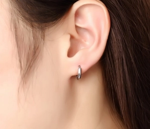 Gros plan d'une boucle d'oreille créole en argent minimaliste sur une oreille polie
