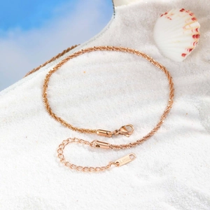 Détail de la chaîne torsadée en acier inoxydable or rose sur sable avec coquillage et fermoir