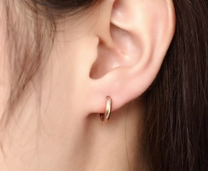 Gros plan macro d'une boucle d'oreille créole en acier titane rose doré portée