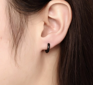 Gros plan d'une boucle d'oreille minimaliste en acier titane noir portée par une femme