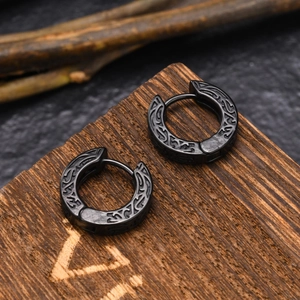 Engraved black stainless steel hoop earrings with vintage pattern on a wooden surface