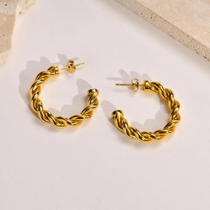 Détail de boucles d'oreilles créoles torsadées dorées avec une finition polie brillante