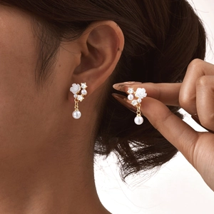 Close-up of golden camellia earrings with white pearls and crystals worn by a model