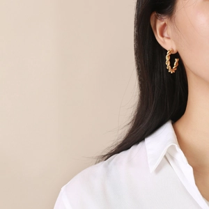Gros plan de boucles d'oreilles créoles dorées torsadées portées avec style minimaliste