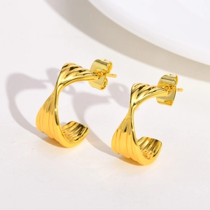 Close-up of golden C-shaped twisted hoop earrings with a textured ribbed finish
