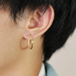 Gros plan d'une créole dorée polie minimaliste portée à l'oreille d'un modèle
