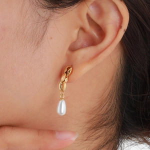 Close-up of golden drop earrings with white pearls worn by a model in natural light