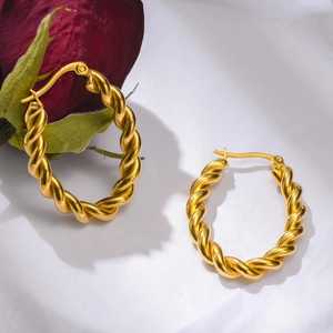 Gros plan de boucles d'oreilles créoles torsadées dorées avec texture de métal tressé poli