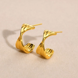 Elegant gold-tone C-shaped twist hoop earrings with ribbed texture on beige velvet