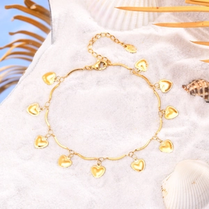 Détail de la chevillère cœur en or 18K sur sable de plage avec coquillages d'été