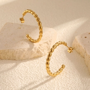 Detailed close-up of golden C-shaped hoop earrings with beaded texture on a stone
