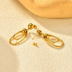 Detail of gold-plated stainless steel hoop earrings with sphere studs on white stone