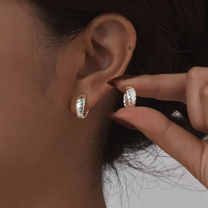 Gros plan de boucles d'oreilles créoles torsadées en métal argenté sur un modèle