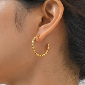 Close-up of woman wearing golden C-shaped hoop earrings with beaded texture and metal luster