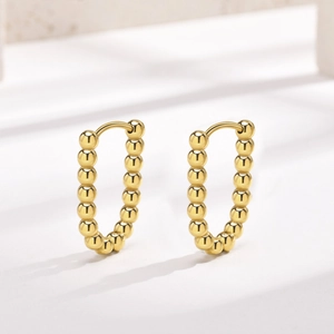 Macro shot of 18K gold plated beaded U-shape hoop earrings on a light marble surface
