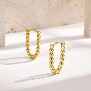 Detail shot of 18K gold plated beaded U-shape earrings on a minimalist stone background