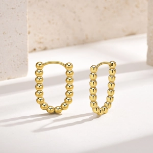 Detail of 18K gold plated beaded U-shaped hoop earrings on a stone textured display