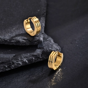 Macro shot of gold hoop earrings with triple groove texture on black rock surface